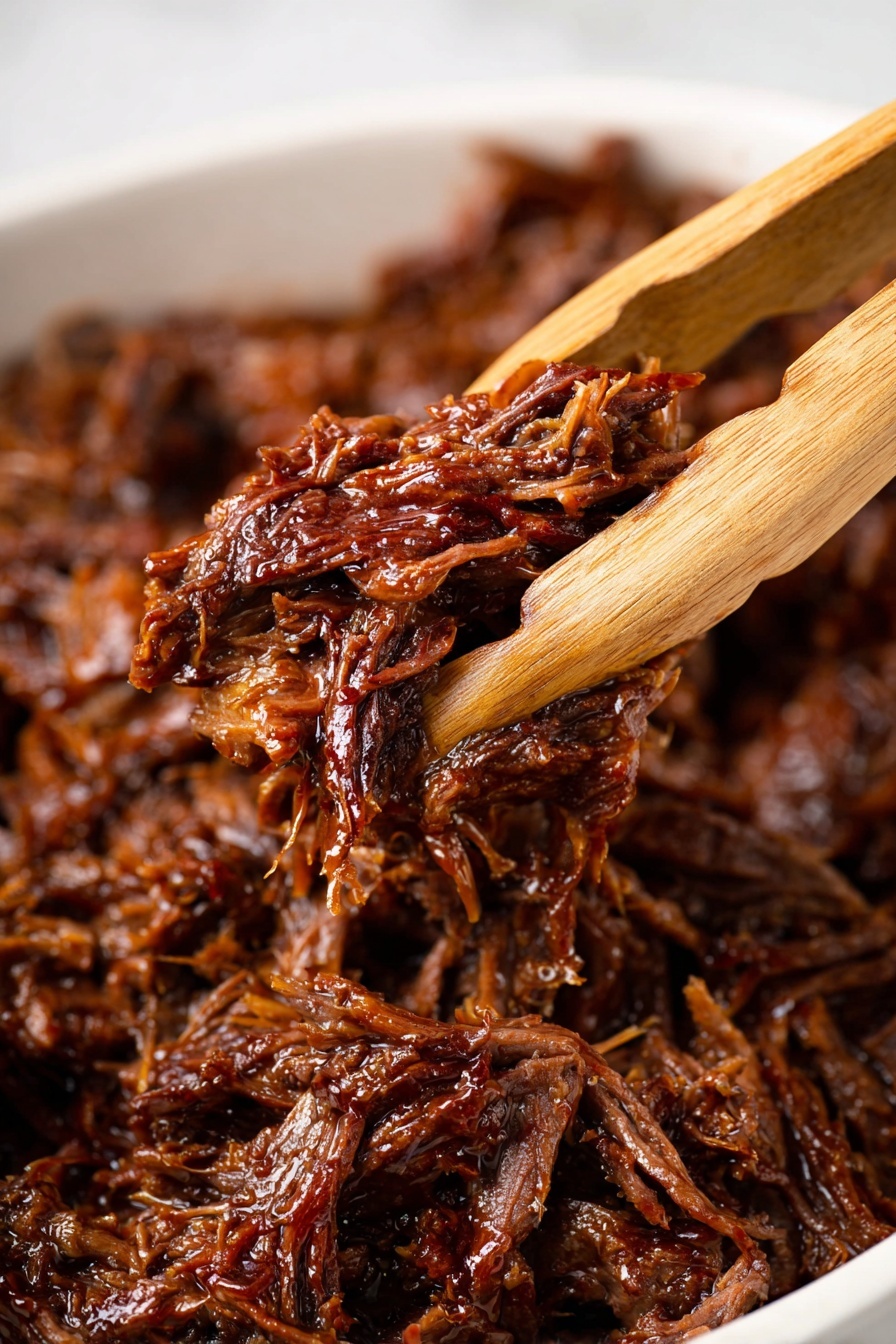 A close-up of shredded meat with a rich, dark brown color and shiny, moist texture, held by wooden tongs in the center of the image; background shows more shredded meat piled together, all resting on a white marbled surface. photo taken with an iphone --ar 2:3 --v 7