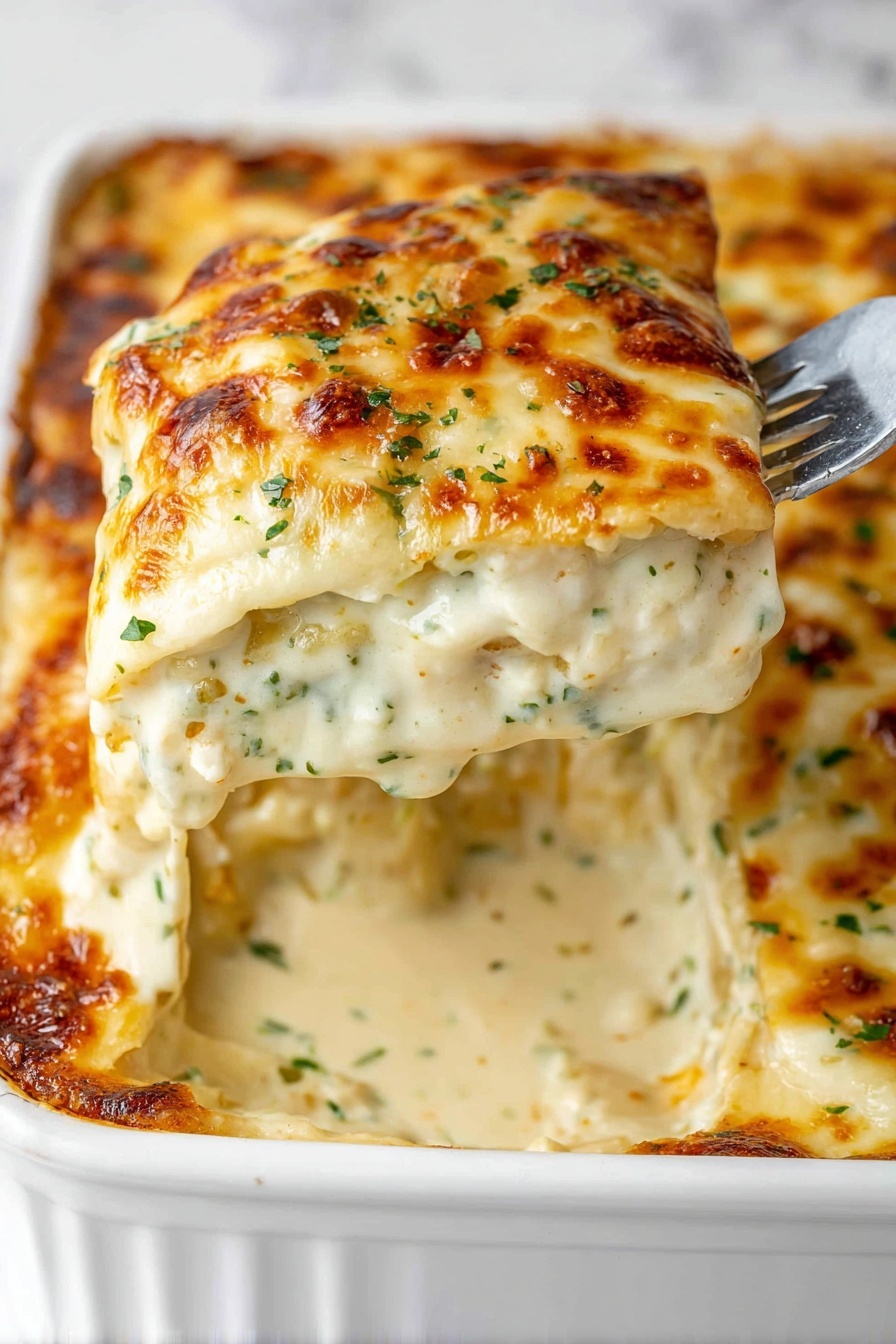 A close-up of a creamy baked dish held by a fork above a white baking dish, showing multiple layers of soft pasta sheets covered with thick white sauce with green herbs and small bits of ingredients, topped with golden-brown melted cheese that looks slightly crispy and bubbly, with threads of melted cheese dripping from the lifted piece. The background is a white marbled surface. photo taken with an iphone --ar 2:3 --v 7