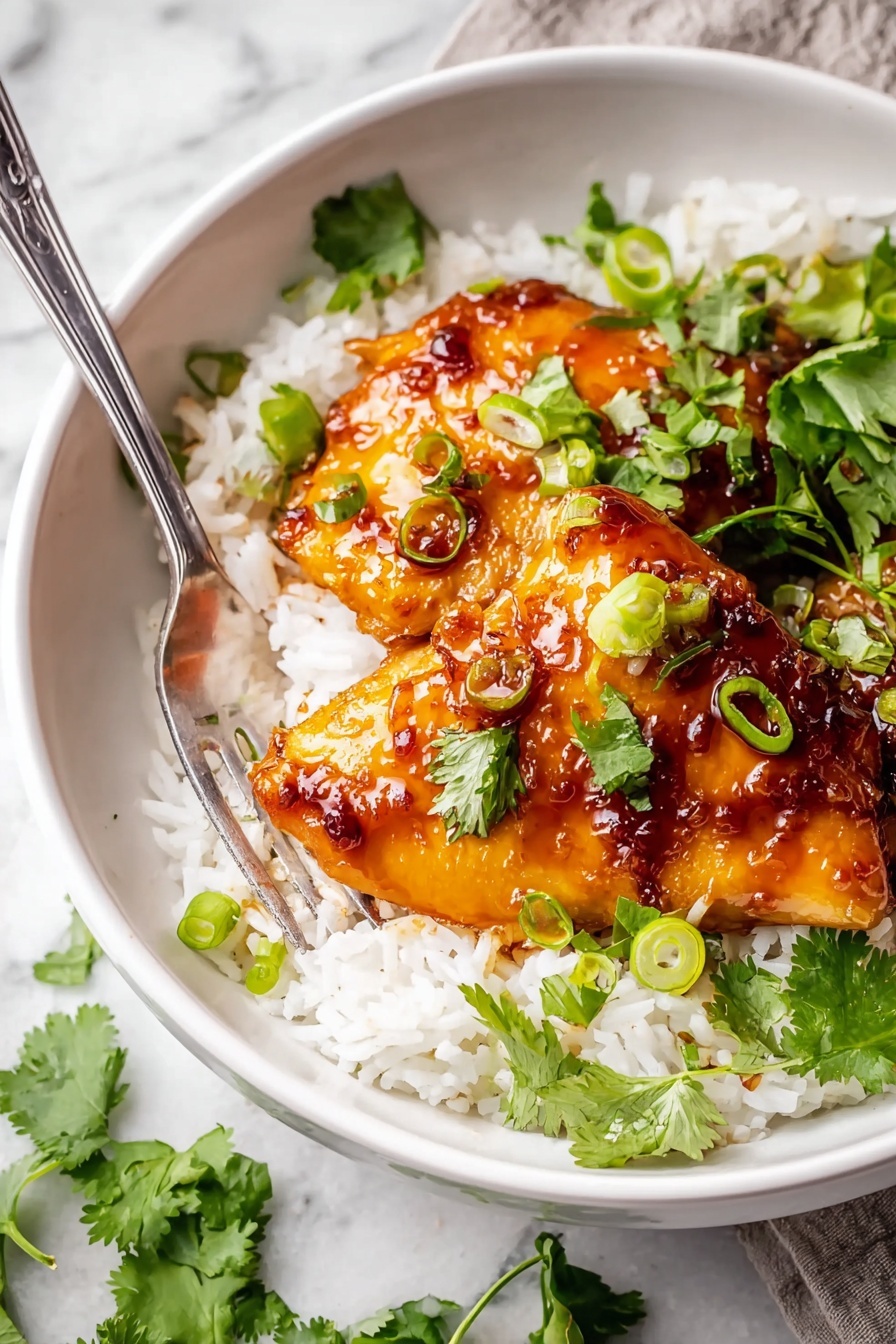 A white bowl filled with a base layer of fluffy white rice topped with three pieces of glossy, golden-brown glazed chicken thighs covered in a thick, shiny, dark orange-red sauce. The chicken is garnished with bright green sliced scallions and fresh cilantro leaves scattered on top and around. A silver fork rests on the left side of the bowl, and the bowl sits on a white marbled surface with some scattered green cilantro leaves nearby. photo taken with an iphone --ar 2:3 --v 7