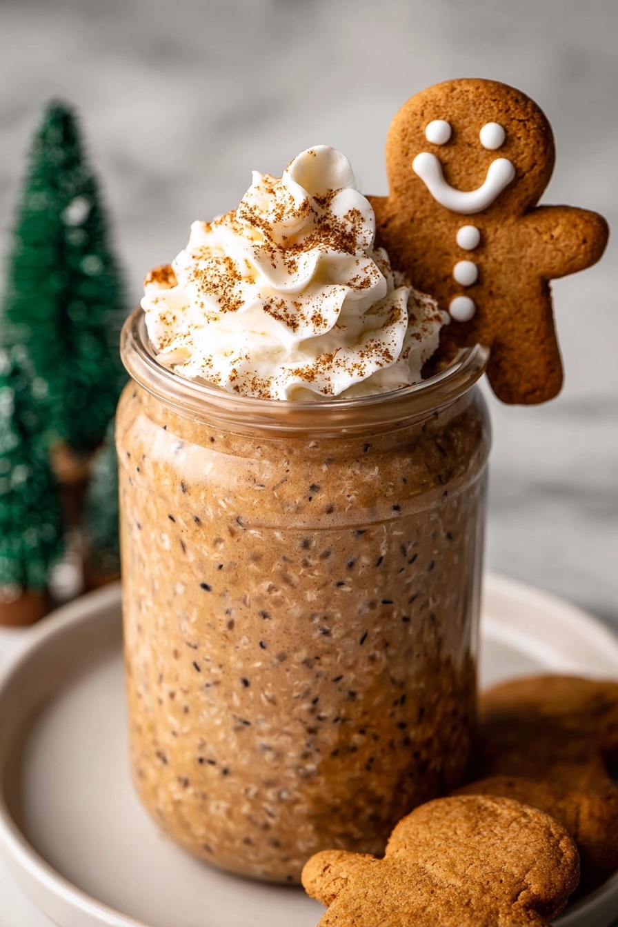 A clear glass jar is filled with a thick, textured light brown drink or pudding that shows small darker flecks throughout, topped with a swirl of white whipped cream sprinkled with light brown powder. A gingerbread cookie shaped like a smiling person with white icing eyes, mouth, and squiggles on the arms and lower body stands upright inside the jar, leaning on the whipped cream. The jar sits on a round white plate on a white marbled surface, with another gingerbread cookie partially visible on the plate near the bottom left. Soft-focus green miniature tree decorations are in the background. Photo taken with an iphone --ar 2:3 --v 7
