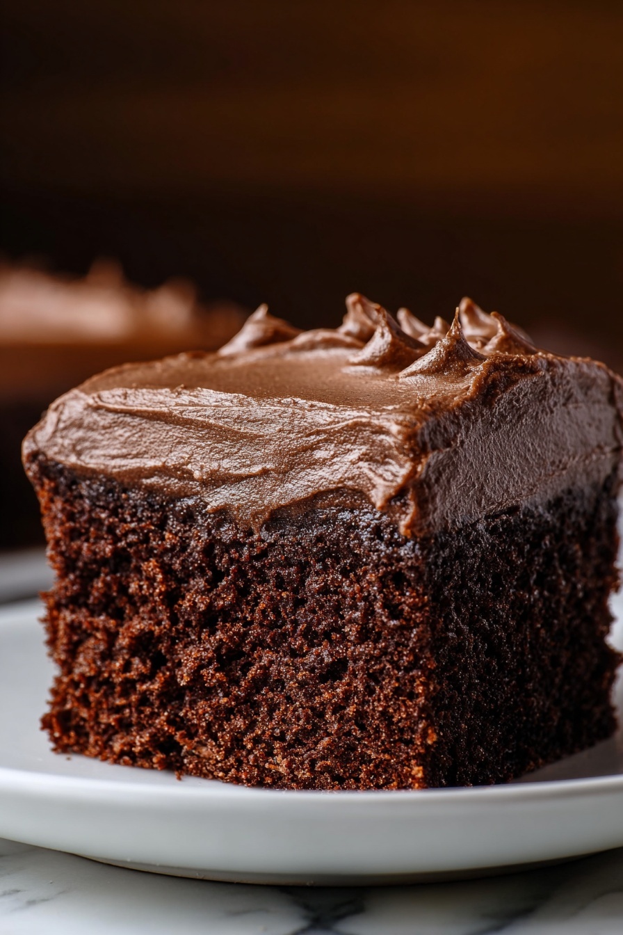 A close-up view of a single square piece of chocolate cake with two layers: the bottom layer is a rich, dark brown, soft, and moist cake, and the top layer is a thick, smooth, creamy chocolate frosting with slightly wavy texture. The cake sits on a white plate against a blurred brown background that blends softly with the cake's dark color. The edges of the cake are slightly uneven, showing the softness of the frosting on top. The surface beneath the plate is white marble texture. photo taken with an iphone --ar 2:3 --v 7