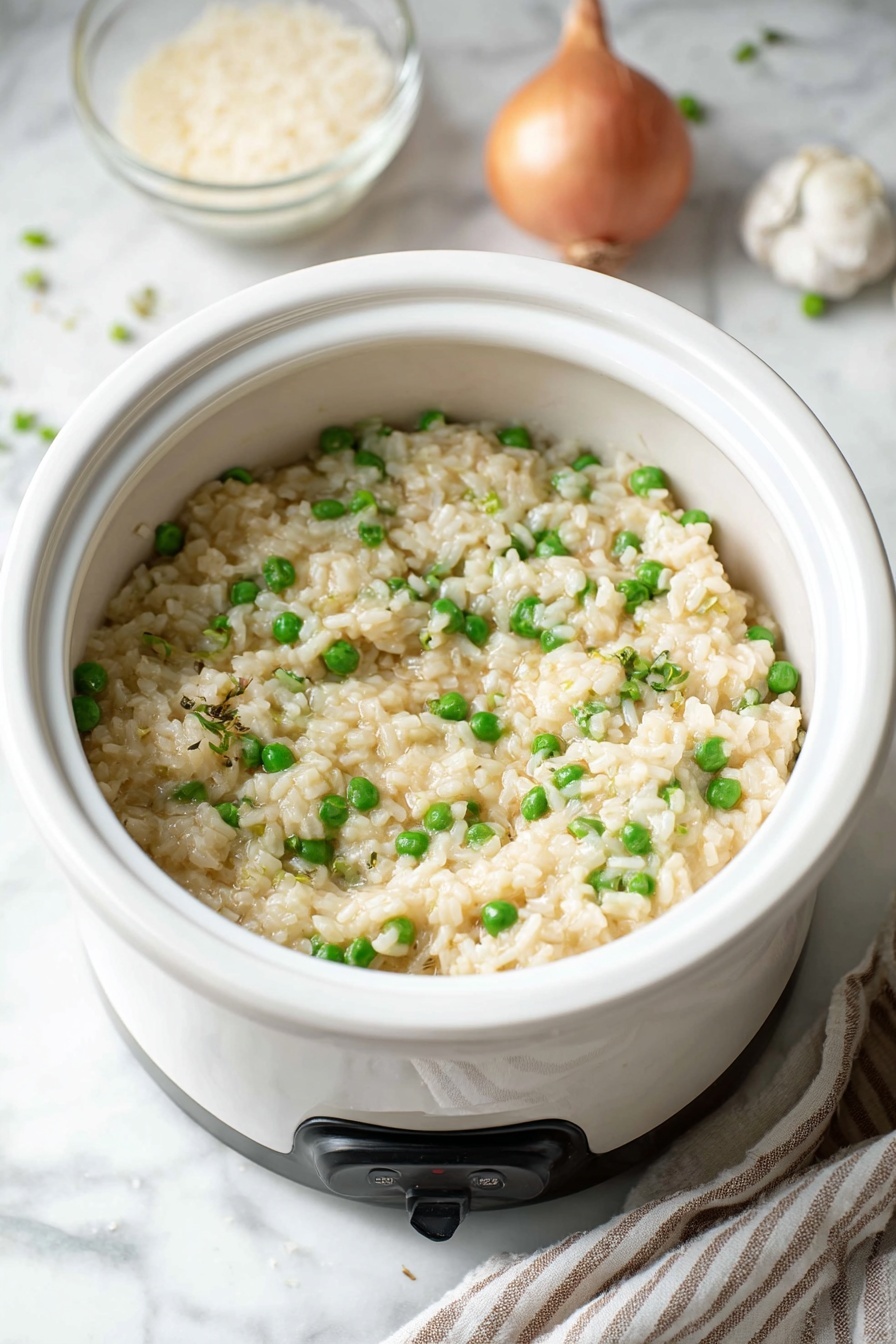 A white bowl filled with creamy risotto showing soft, pale yellow rice mixed with bright green peas evenly spread throughout. The risotto looks moist and slightly chunky, with small bits of onion visible among the rice. Light black pepper is sprinkled on the top, adding small dark specks across the dish. The bowl sits on a white marbled surface with a clear glass bowl of raw rice, a whole garlic bulb, some cheese shavings, and a shallot placed nearby. A white rice cooker with warm and cook indicator lights is partially visible on the right side. Photo taken with an iphone --ar 2:3 --v 7
