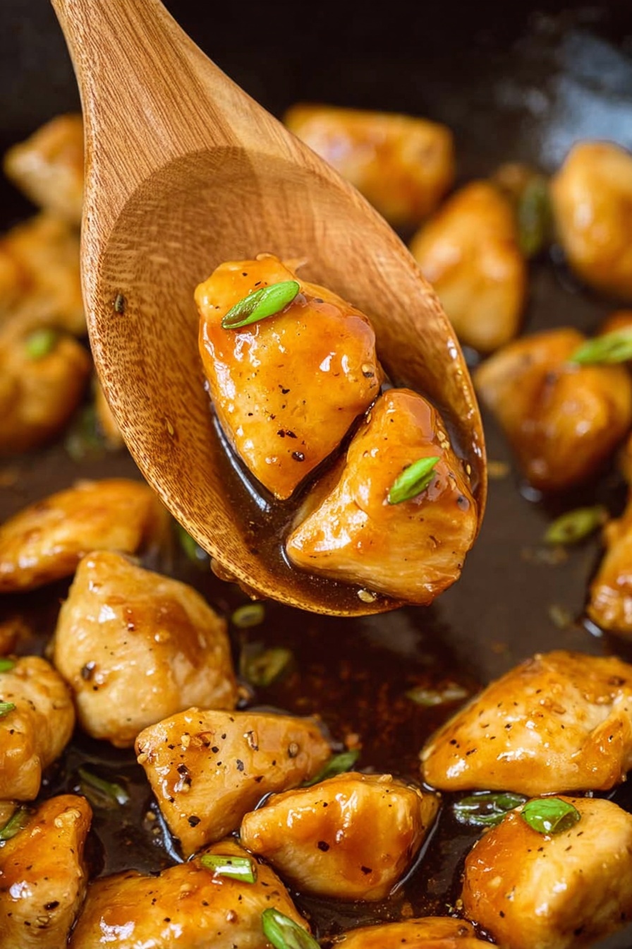 The image shows a wooden spoon holding two shiny, golden brown pieces of cooked chicken coated in a thick, glossy brown sauce with small black pepper specks and sliced green onions. Below the spoon is a pan filled with more pieces of chicken in the same sauce scattered unevenly, with a few green onion slices visible. The background has a white marbled texture. photo taken with an iphone --ar 2:3 --v 7