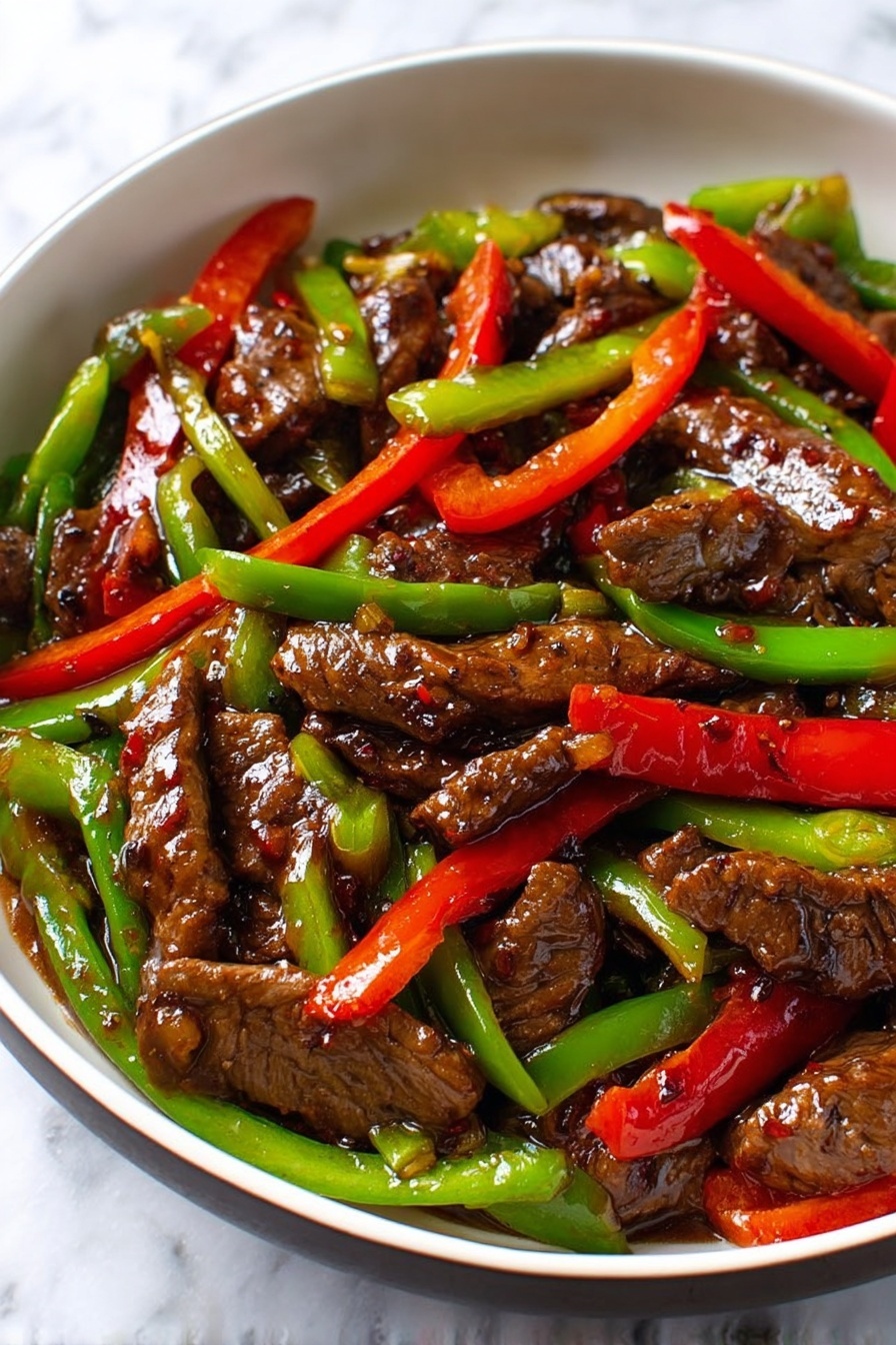 This close-up image shows a stir-fry dish in a white bowl, filled mainly with dark brown pieces of beef that are glossy and covered in sauce. Mixed in are bright, crisp strips of red and green bell peppers, cut into long sticks, spread evenly on and around the beef. The beef looks tender with a shiny texture from the sauce, which adds a slight wet look to the whole dish. The background is a white marbled surface, and the colors of the peppers and beef stand out clearly. photo taken with an iphone --ar 2:3 --v 7