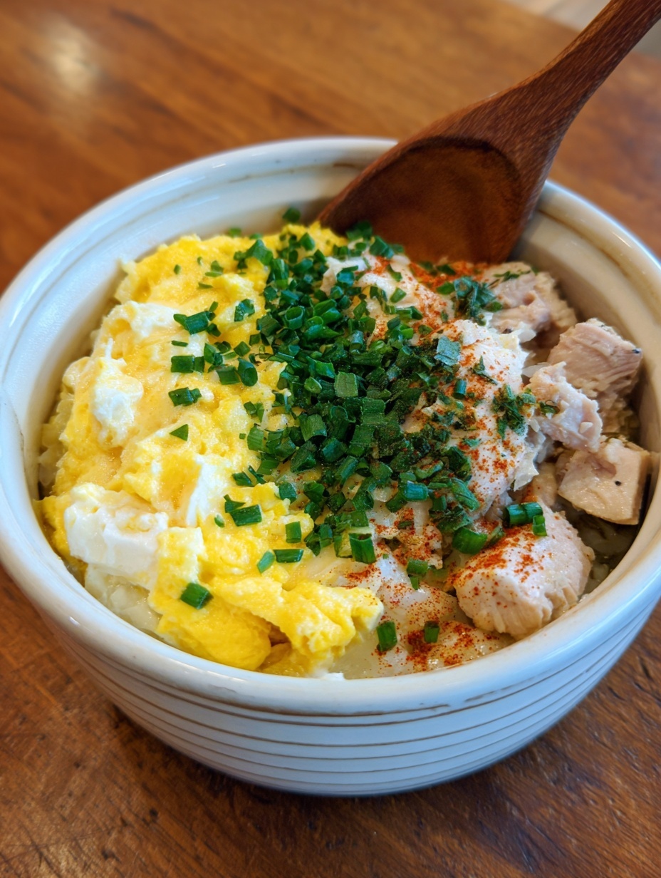 The image shows a black bowl filled with white fluffy rice as the base layer. On top of the rice is a golden-brown cooked egg layer mixed with cooked green onions and thin brown onion slices, scattered across the surface. A few larger green onion pieces sit on top, adding bright green color contrast. The bowl is placed on a white marbled surface, with a blue glass on the side and part of a beige cloth with a blue stripe visible at the edge. photo taken with an iphone --ar 2:3 --v 7