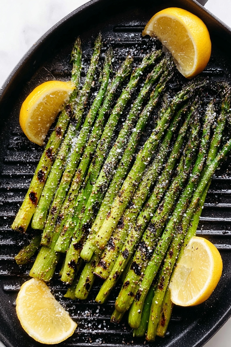 A black round grill pan filled with a single layer of grilled green asparagus spears placed side by side, showing some charred dark lines and lightly sprinkled with coarse salt and cracked black pepper. Three lemon wedges with slightly charred spots are placed on the right and bottom edges of the pan, adding bright yellow contrast. The pan sits on a white marbled surface. photo taken with an iphone --ar 2:3 --v 7