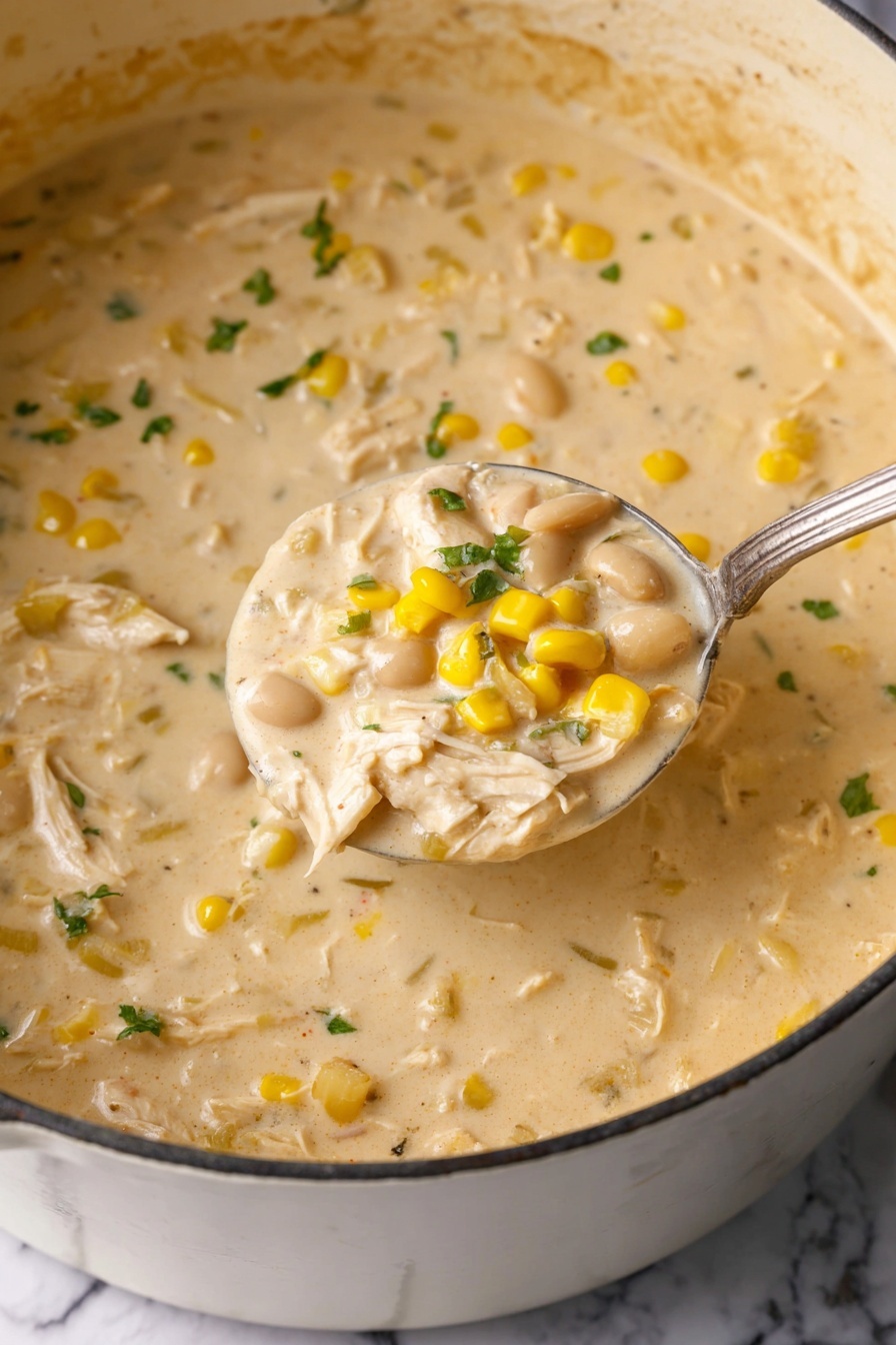 A close-up of a large white pot filled with creamy chicken corn chowder, showing about four layers: a thick pale yellow broth full of shredded light beige chicken, bright yellow corn kernels, and pale white beans mixed throughout, with bits of green herbs scattered on top. A metal ladle lifts a scoop of the chowder, highlighting the chunky texture and the rich, smooth creamy base. The background is a white marbled surface. Photo taken with an iphone --ar 2:3 --v 7