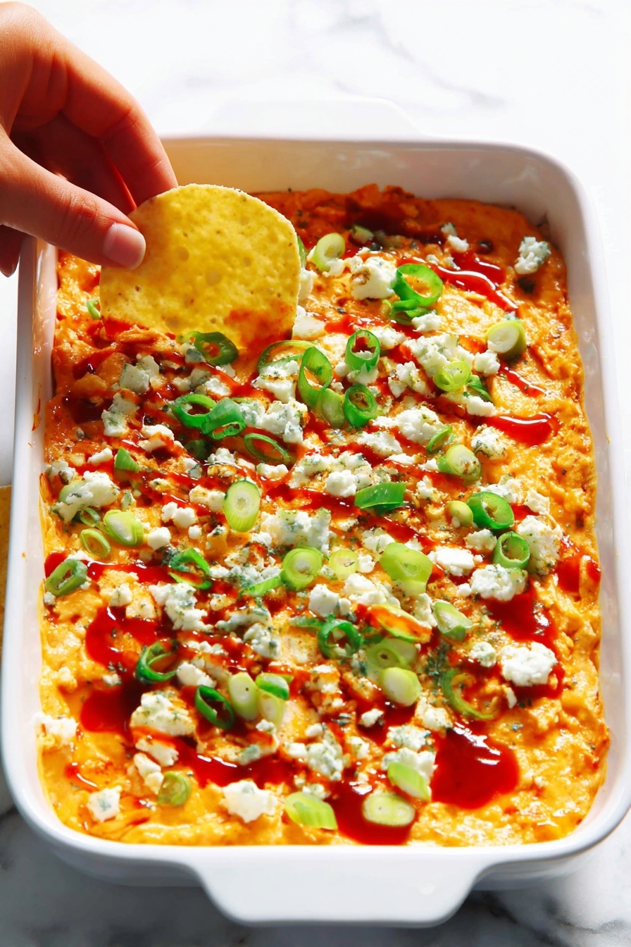 The image shows a clear glass bowl filled with a thick, creamy orange mixture that has small bits of what seems like shredded ingredients and tiny green specks mixed in. A red and black spatula is partially immersed in the mixture, its red silicone tip covered with the textured blend. The bowl rests on a white marbled surface, and the mixture appears well stirred with a slightly chunky texture and uniform orange color with light patches. photo taken with an iphone --ar 2:3 --v 7